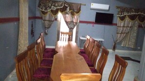 Un espace repas comprenant une longue table en bois et des chaises, une petite table blanche et un téléviseur fixé au mur.