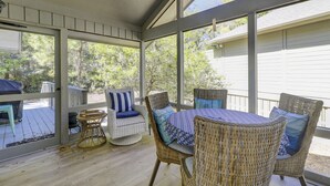 A covered outdoor seating area with wicker furniture and a table, overlooking a garden. - Sunset Rentals | Lawton 45 | Dog Friendly | (Hilton Head Island)