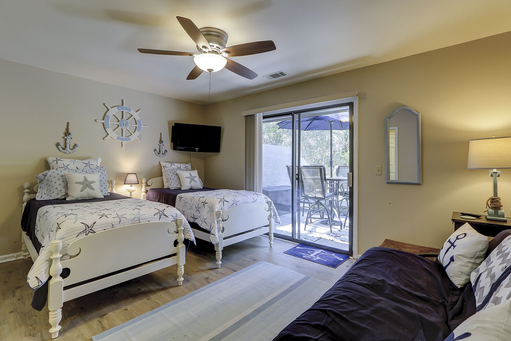 A bedroom with two beds, a ceiling fan, a TV, a sliding glass door to a patio, and a mirror.