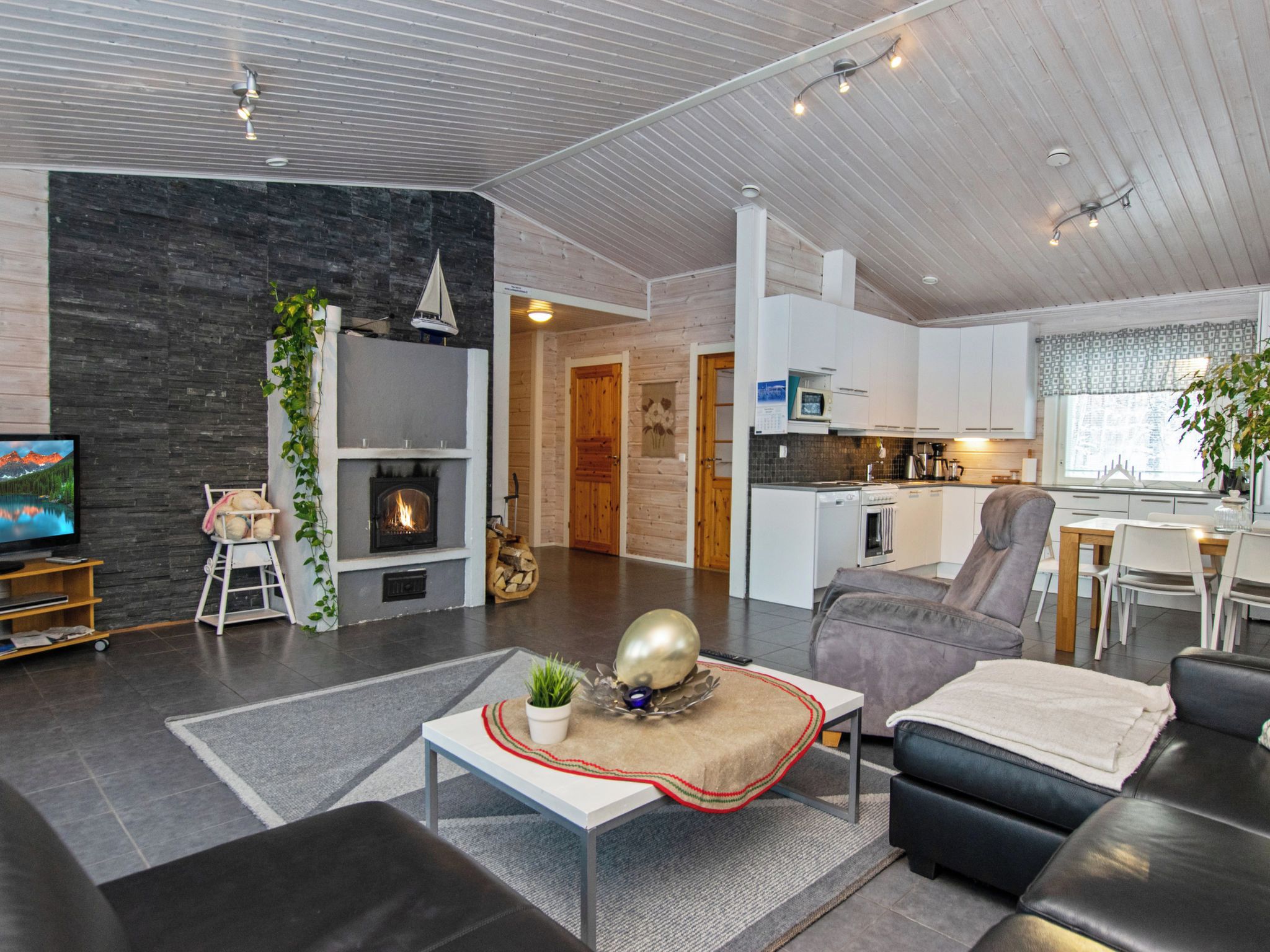 Een moderne woonkamer met een open haard, een televisie en een eetgedeelte, met een keuken op de achtergrond.