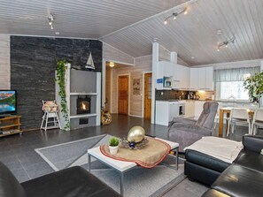 Een moderne woonkamer met een open haard, een televisie en een eetgedeelte, met een keuken op de achtergrond.
