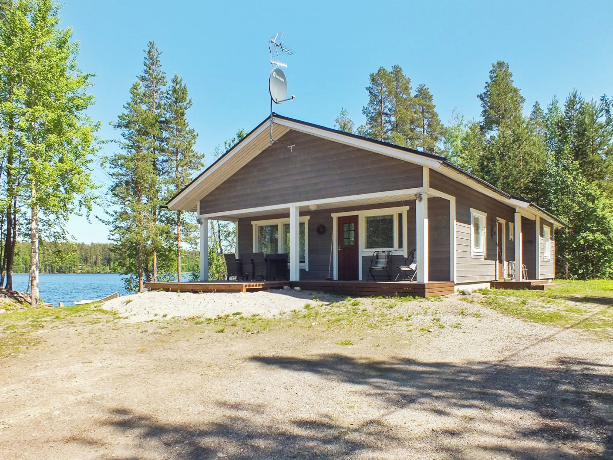 A cabin with a porch, a satellite dish, and a view of a lake.