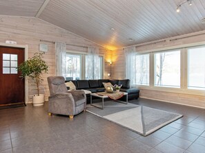 Un salon spacieux comprenant un canapé, un fauteuil et une table basse, de grandes fenêtres et un plafond en bois.