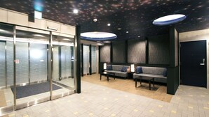 Een ontvangsthal met een glazen lift, een zithoek met banken, en een plafond met sterrenmotief.