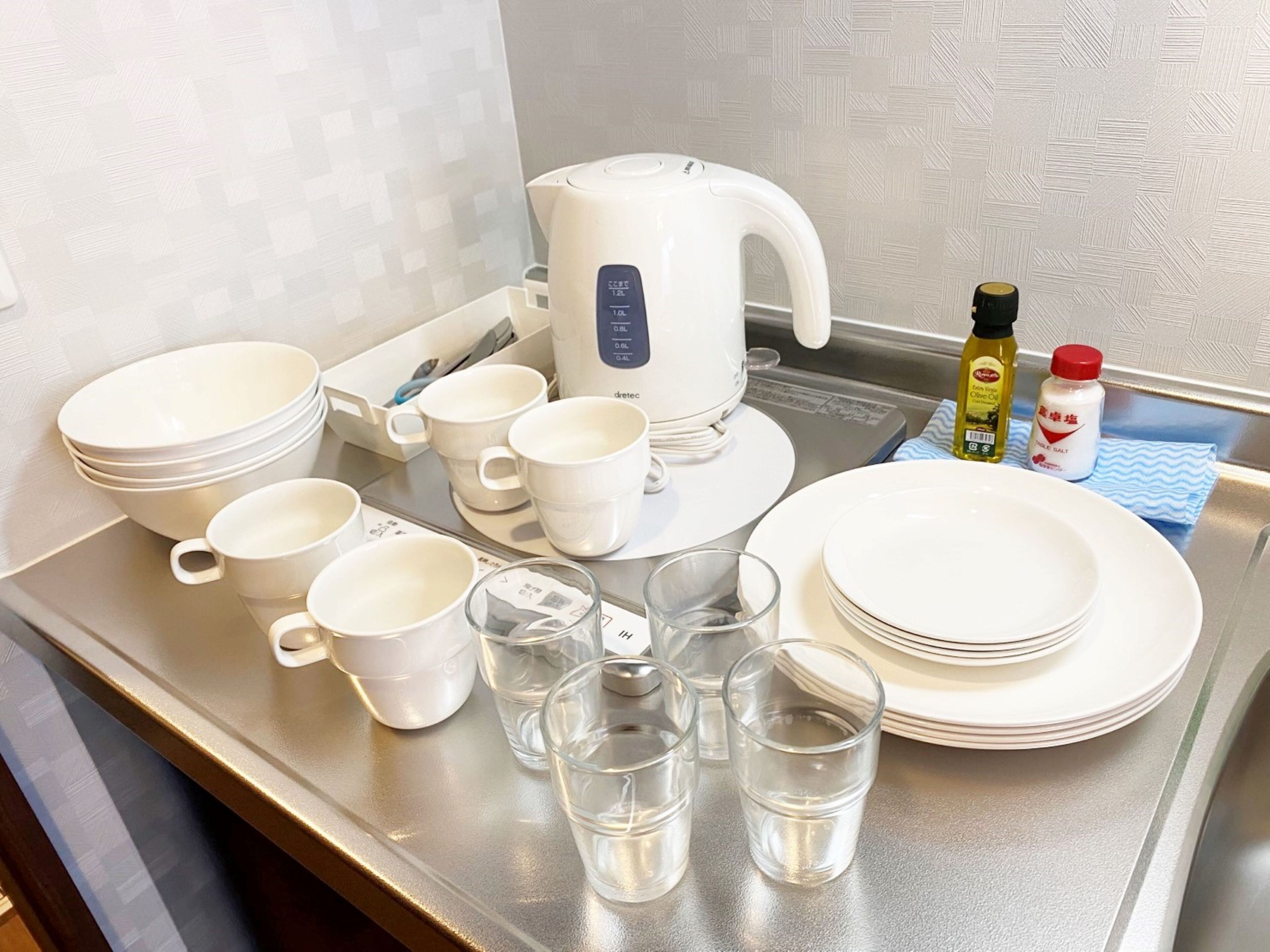 A kitchen counter with a coffee maker, cups, plates, glasses, and condiments.