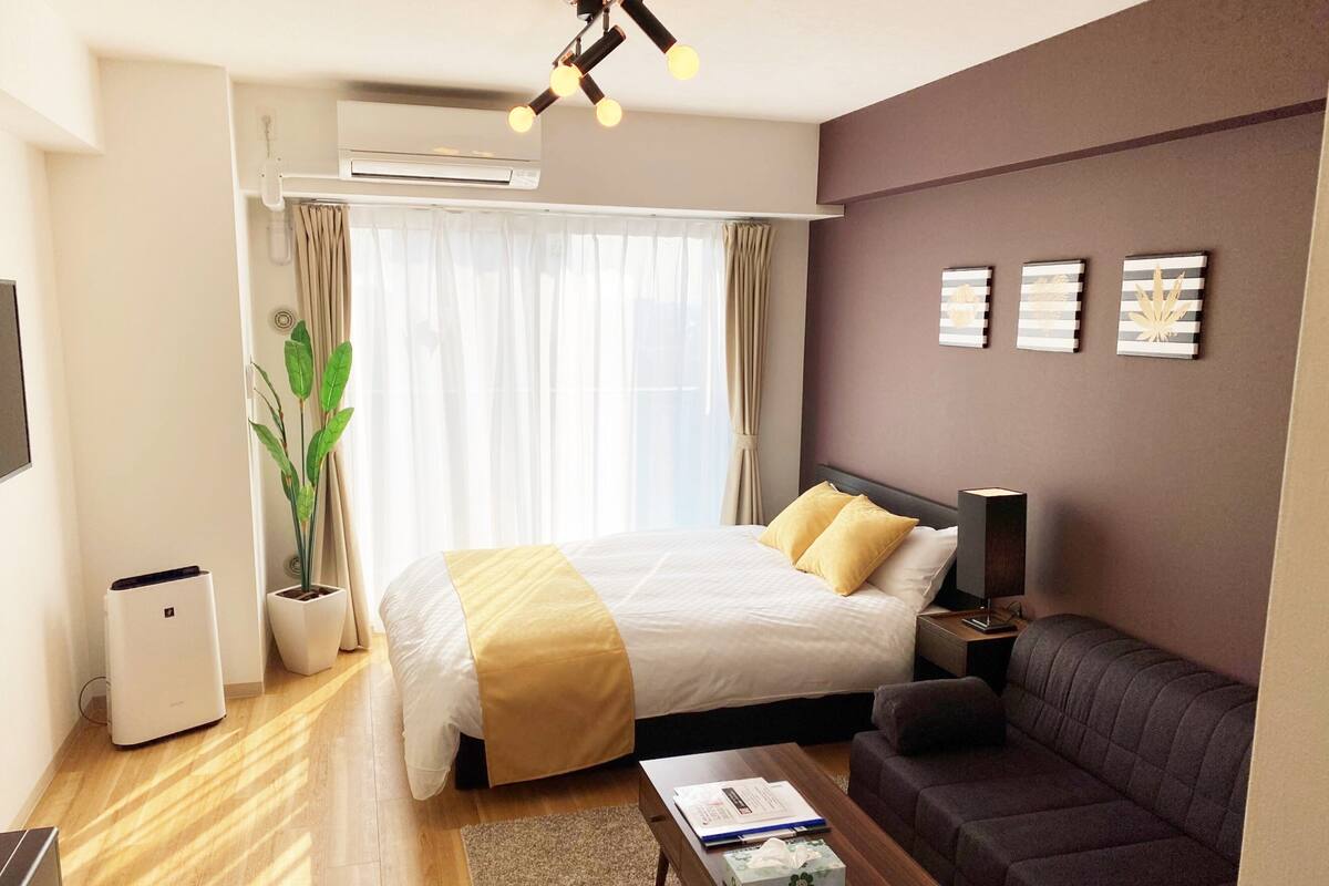 Une chambre d’hôtel moderne avec un lit, un canapé, une table basse et une plante en pot.