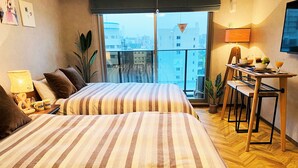 Een hotelkamer met twee bedden, een eettafel, een televisie en uitzicht op de stad.