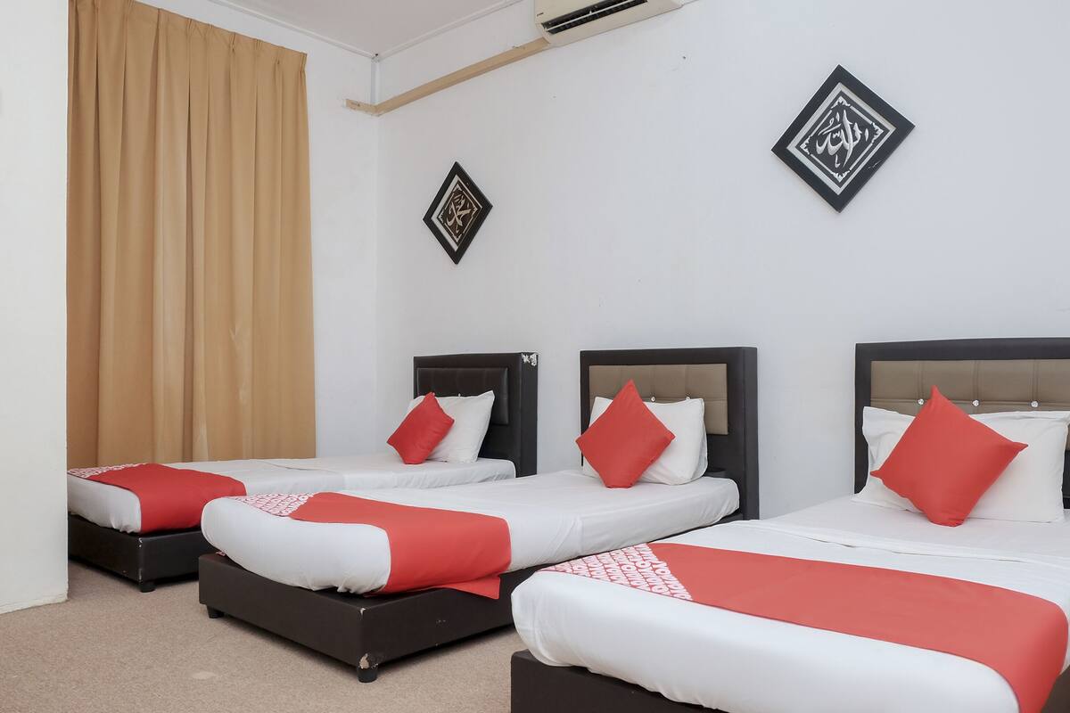 A hotel room with three beds, beige curtains, and two decorative wall pieces.
