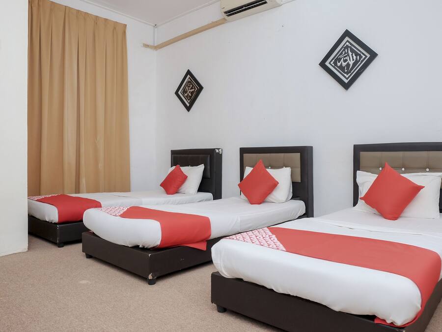 Habitación de hotel con tres camas, cortinas color crema y dos adornos en la pared.