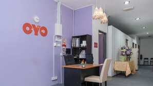 Uma área de recepção com balcão, cadeiras, um relógio e o letreiro 'OYO' na parede.
