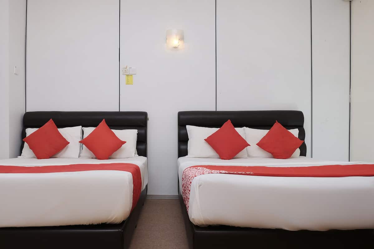 Two beds with black headboards and red pillows, white bedding, and a small wall-mounted light fixture.