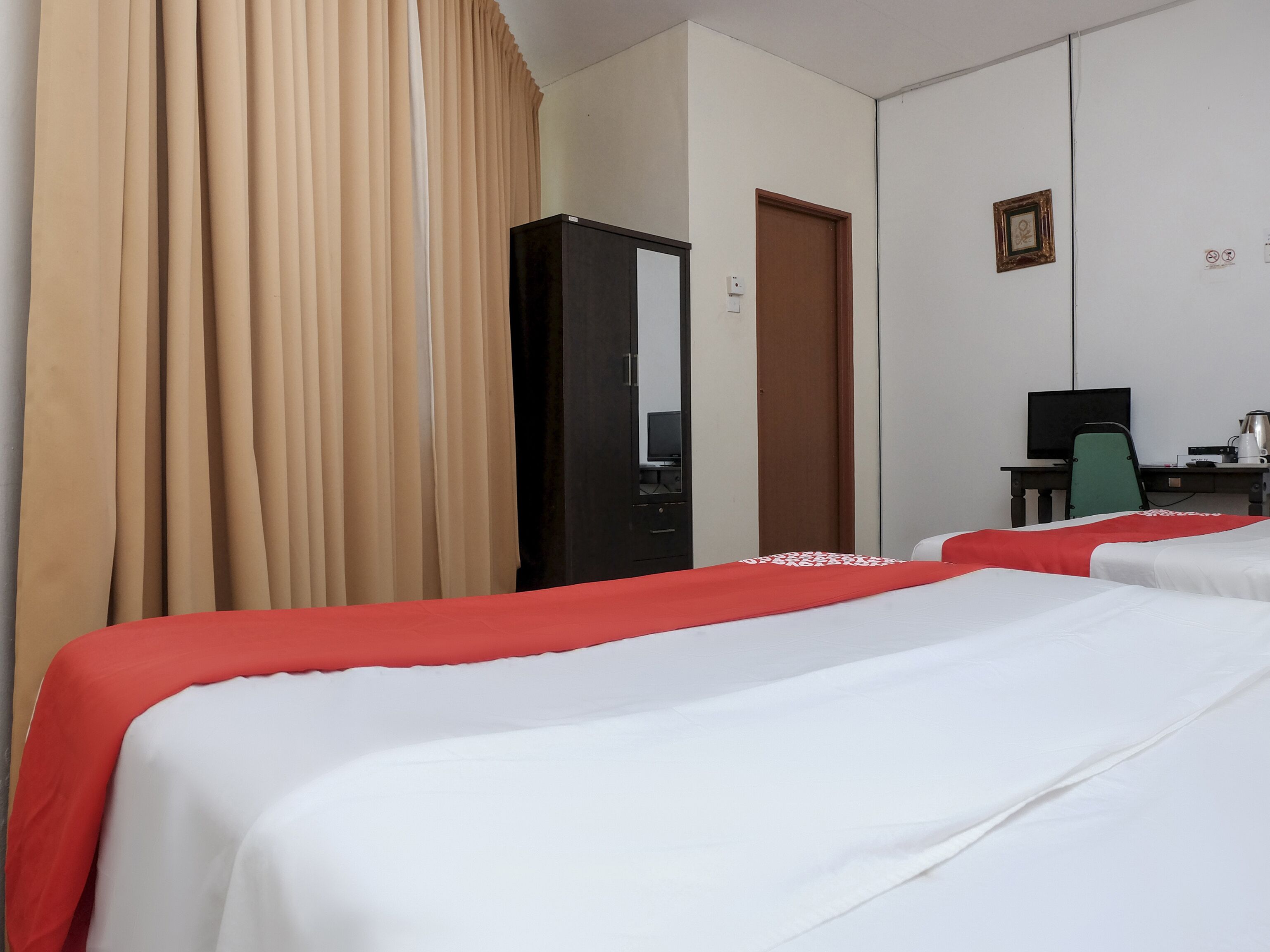 A hotel room with two beds, a desk with a computer, a chair, and a wardrobe.
