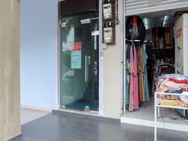Entrada de hotel com porta de vidro, placa indicando reserva de hospedagem e loja de roupas com diversos itens expostos.