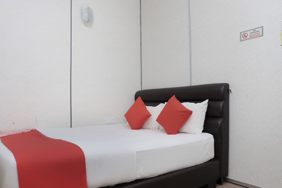 A bed with a black headboard, white bedding, and two red pillows.