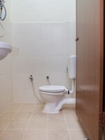 Casa de banho pequena e limpa, com sanita branca, lavatório e chuveiro.