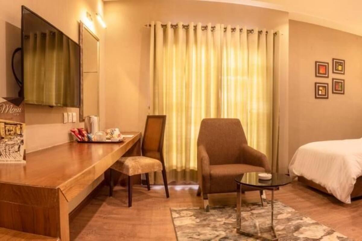 Une chambre d’hôtel avec deux lits, un bureau, une chaise, une petite table et une grande fenêtre avec des rideaux.