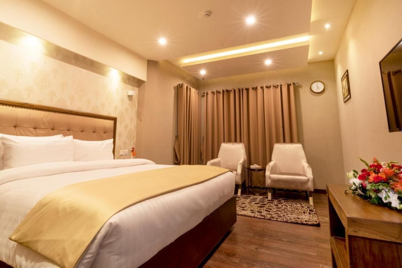 A hotel room with a large bed, two armchairs, a small table, a clock, and a floral arrangement.