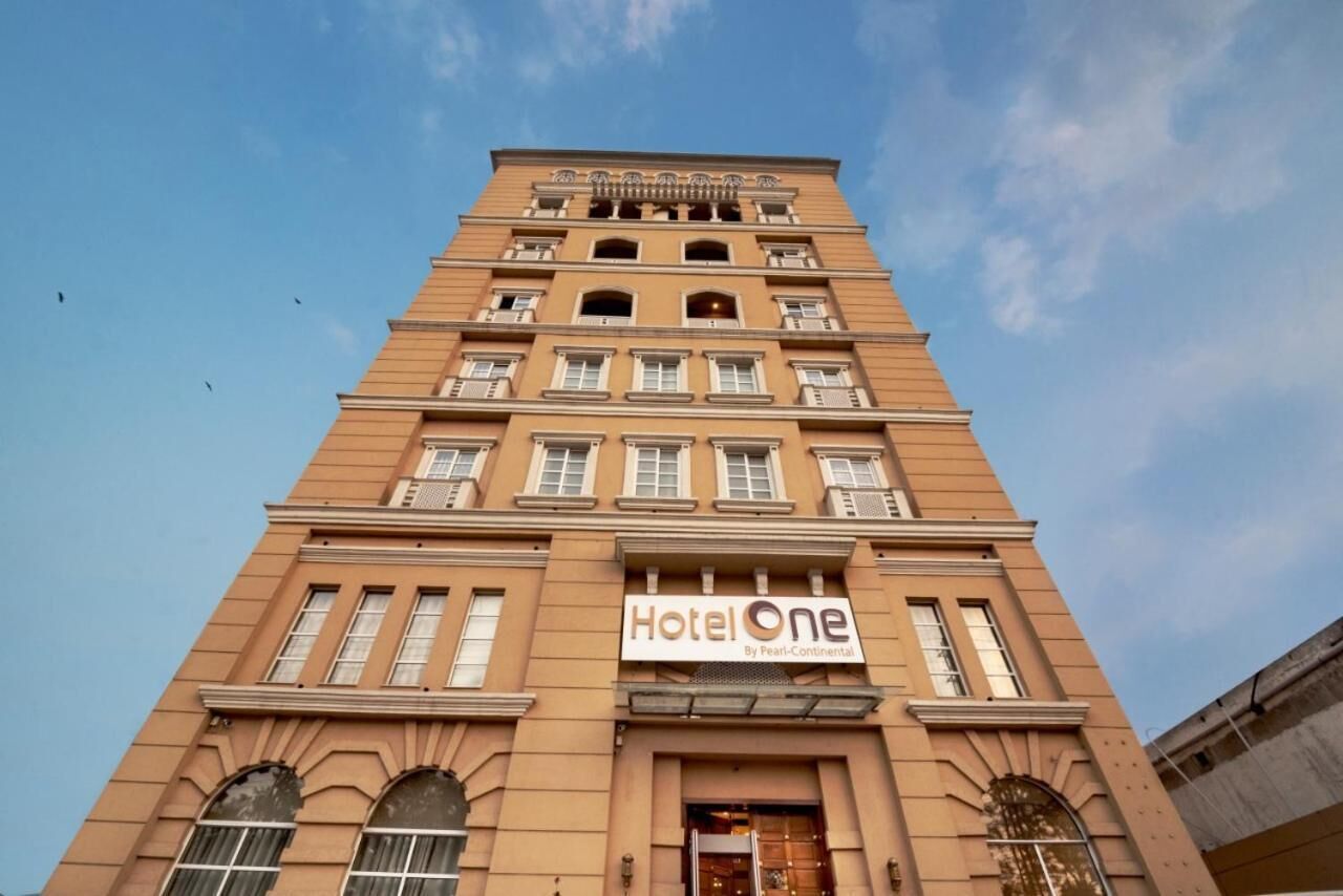 Un grand immeuble de couleur beige, avec l’enseigne « Hotel One » au niveau du rez-de-chaussée.