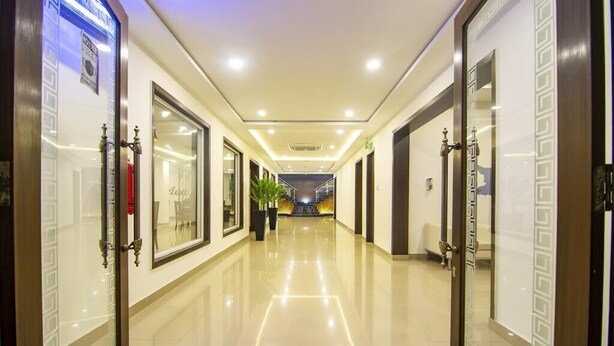 Un pasillo de hotel con un suelo de baldosas brillantes, puertas de cristal con diseños decorativos e iluminación empotrada en el techo.