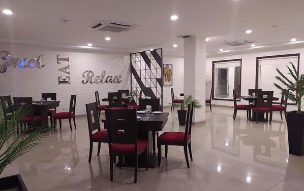 A modern dining area with a white brick wall, a large 'EAT Relax' sign, and several tables with chairs. - Hotel One Sahiwal (Sahiwal)