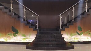 Una escalera moderna con barandillas de vidrio y un rellano central, flanqueada por plantas en macetas.