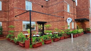 A brick building with a cafe terrace, outdoor seating, and potted plants. - Hotel One Sahiwal (Sahiwal)
