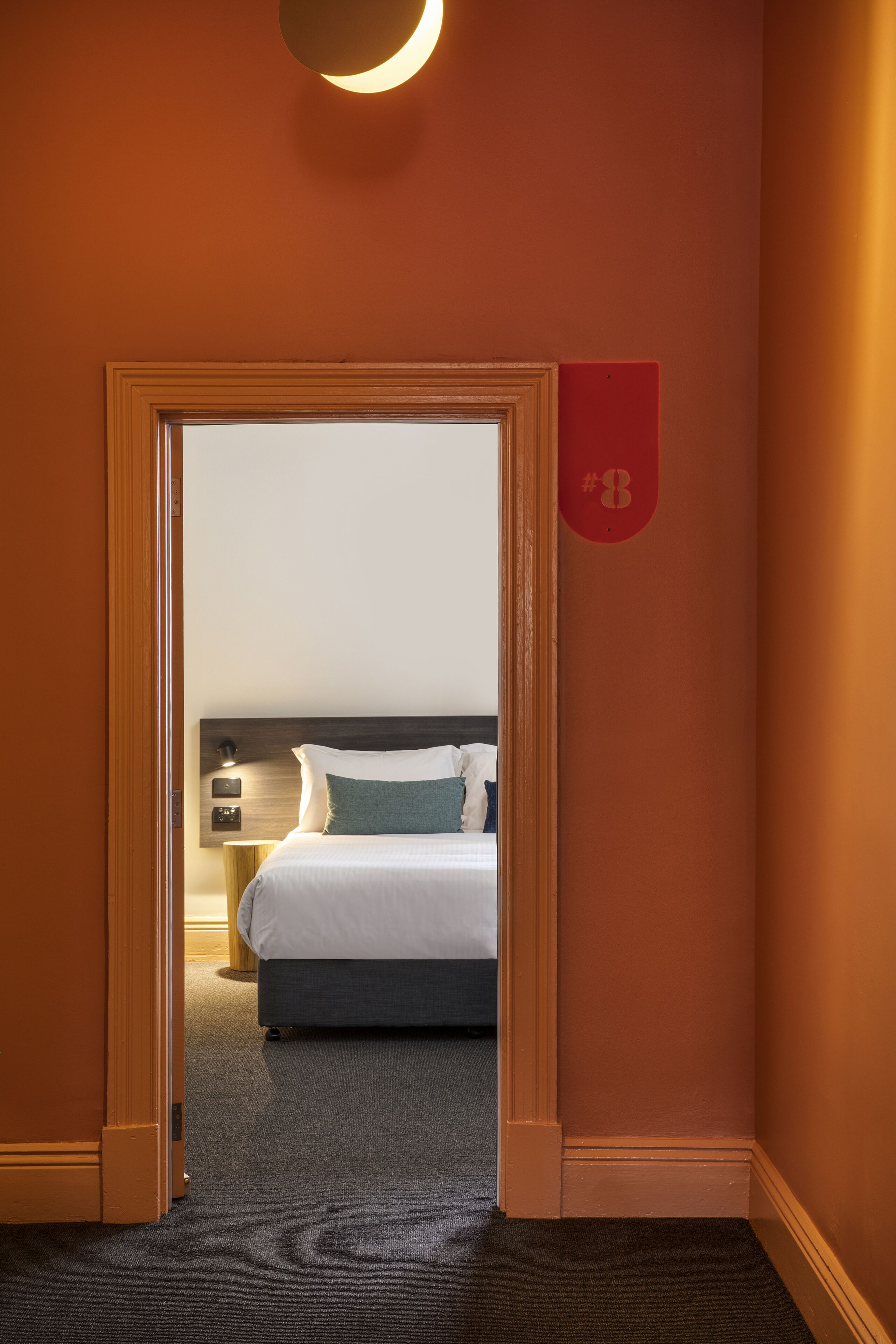 Una habitación de hotel con una cama, una mesita de noche y una lámpara fijada a la pared.