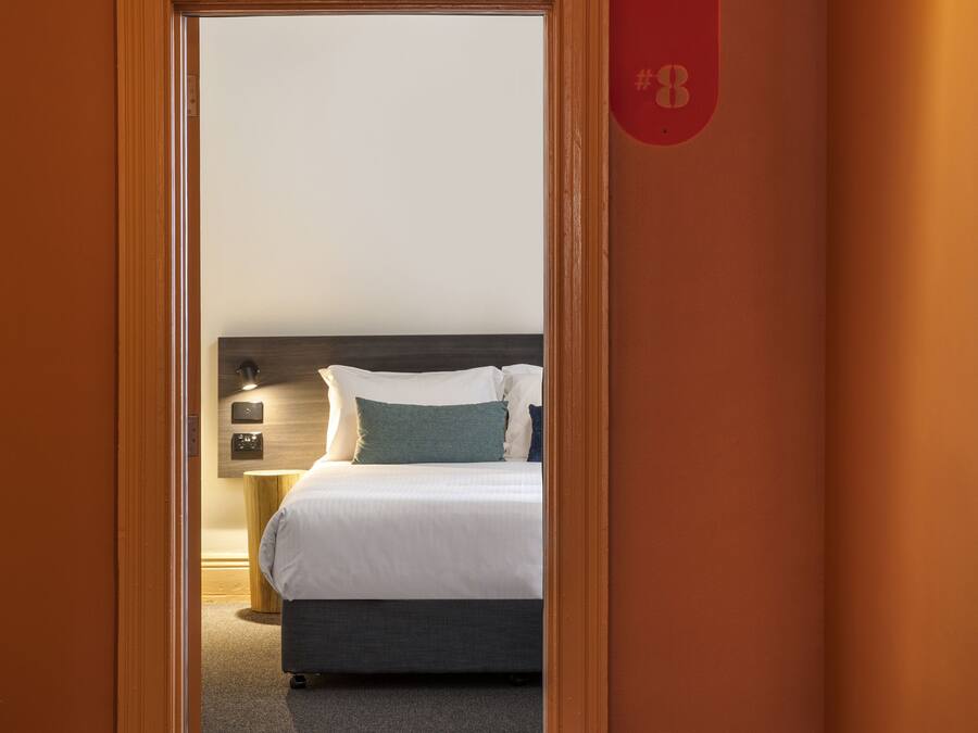 Una habitación de hotel con una cama, una mesita de noche y una lámpara fijada a la pared.