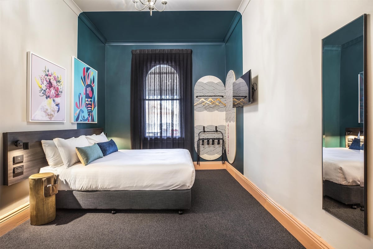 A modern bedroom with a bed, artwork, a mirror, and a unique wall design.