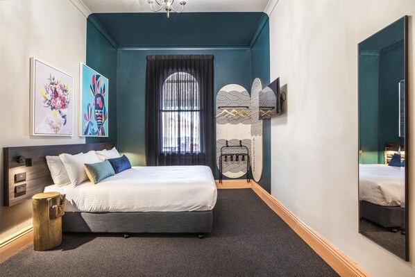 A modern bedroom with a bed, artwork, a mirror, and a unique wall design.