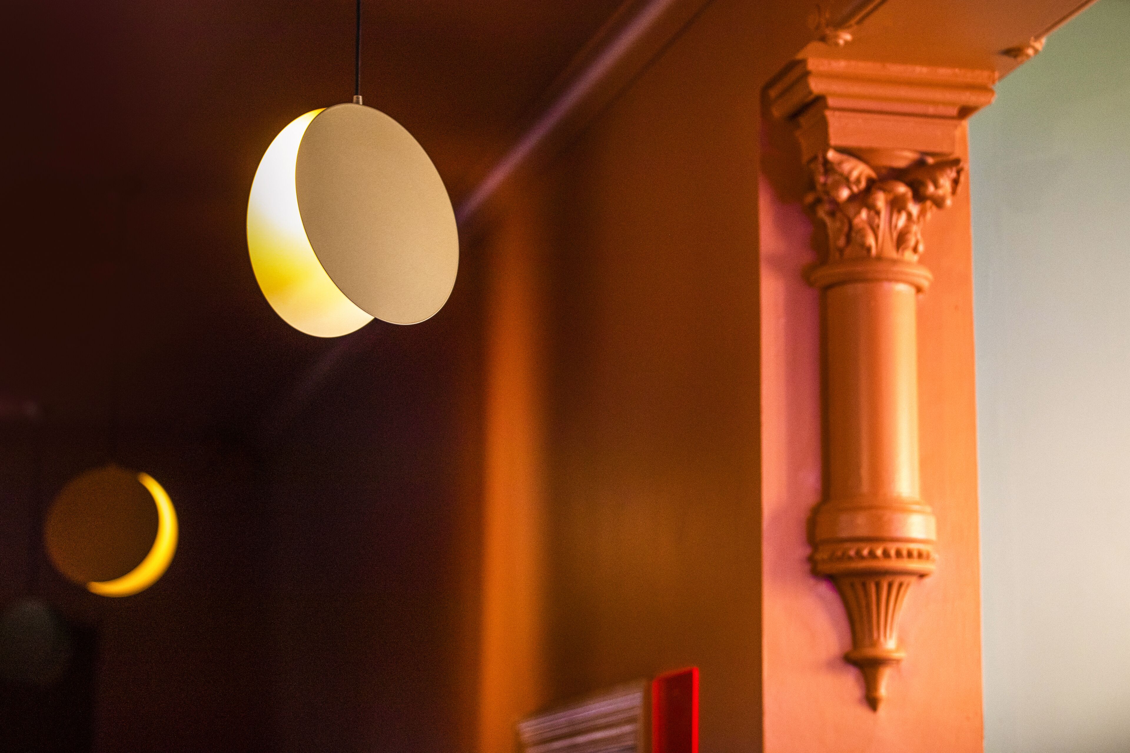 Teto com duas luminárias pendentes esféricas e uma coluna com capitéis ornamentados.
