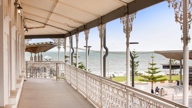 A covered balcony with ornate railings and a view of the sea and a bridge. - Ramsgate Hotel by Nightcap Social (Henley Beach)