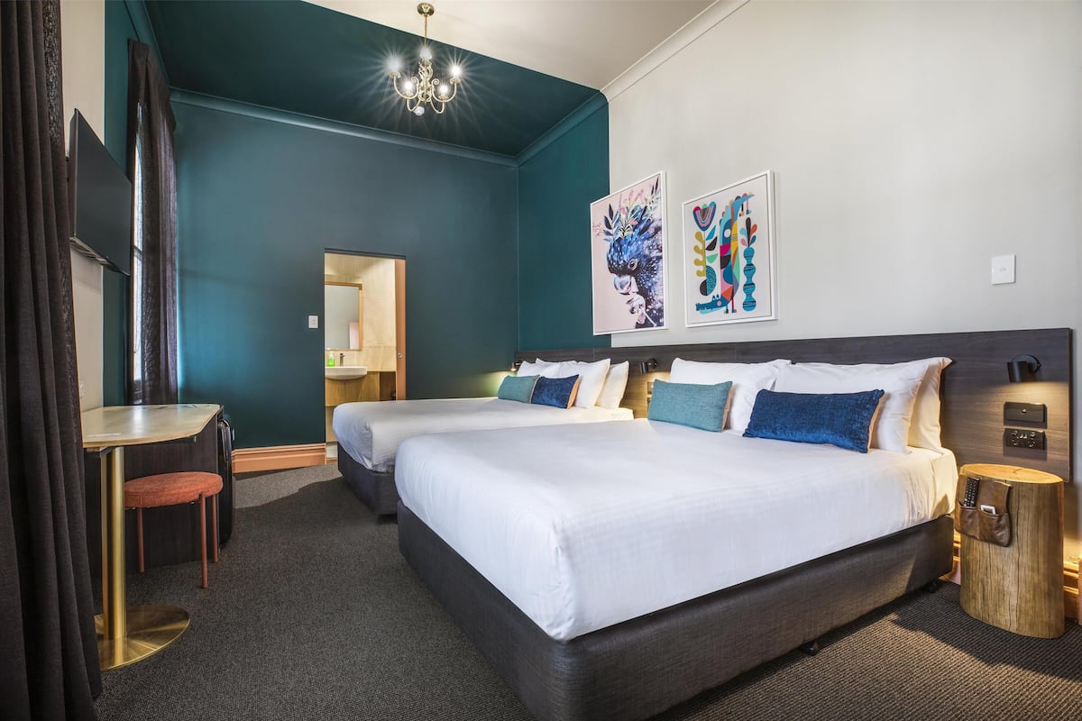 A hotel room with two beds, a desk, a chair, a mirror, and artwork on the walls.