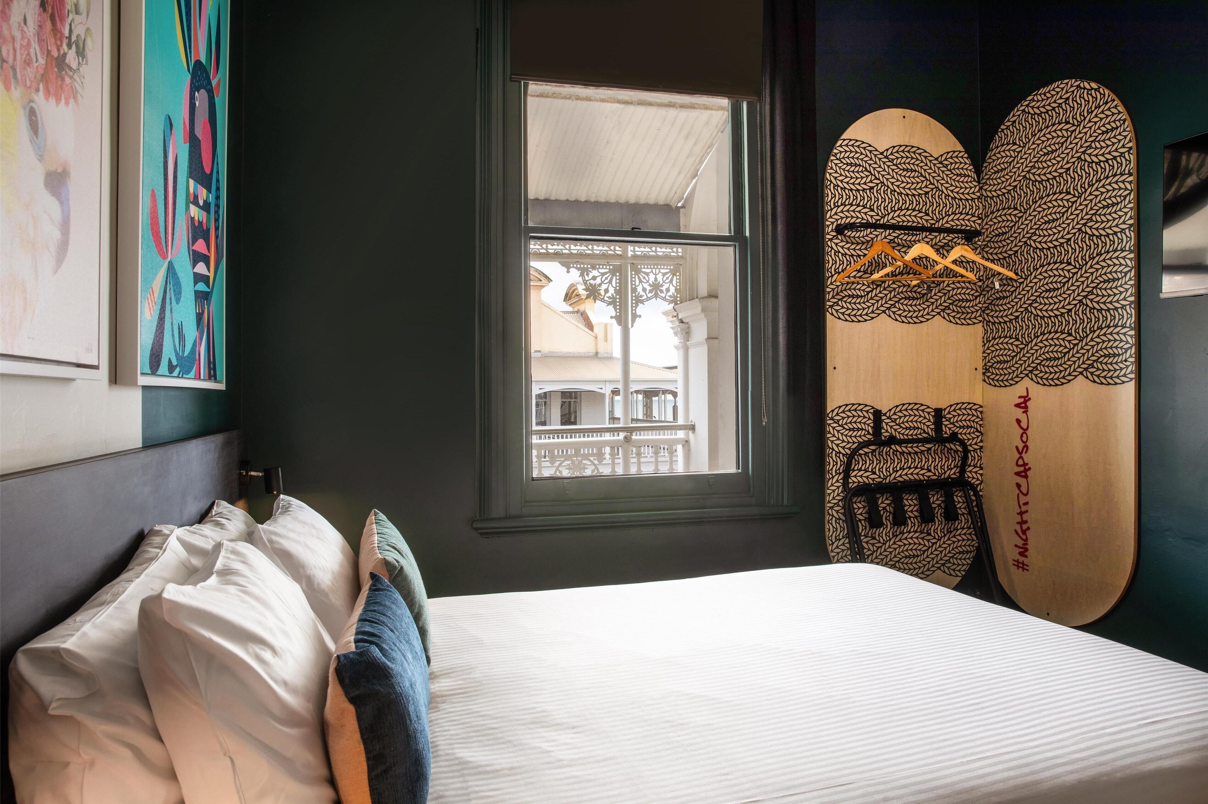Une chambre avec un lit, une fenêtre et deux planches de surf appuyées contre le mur.