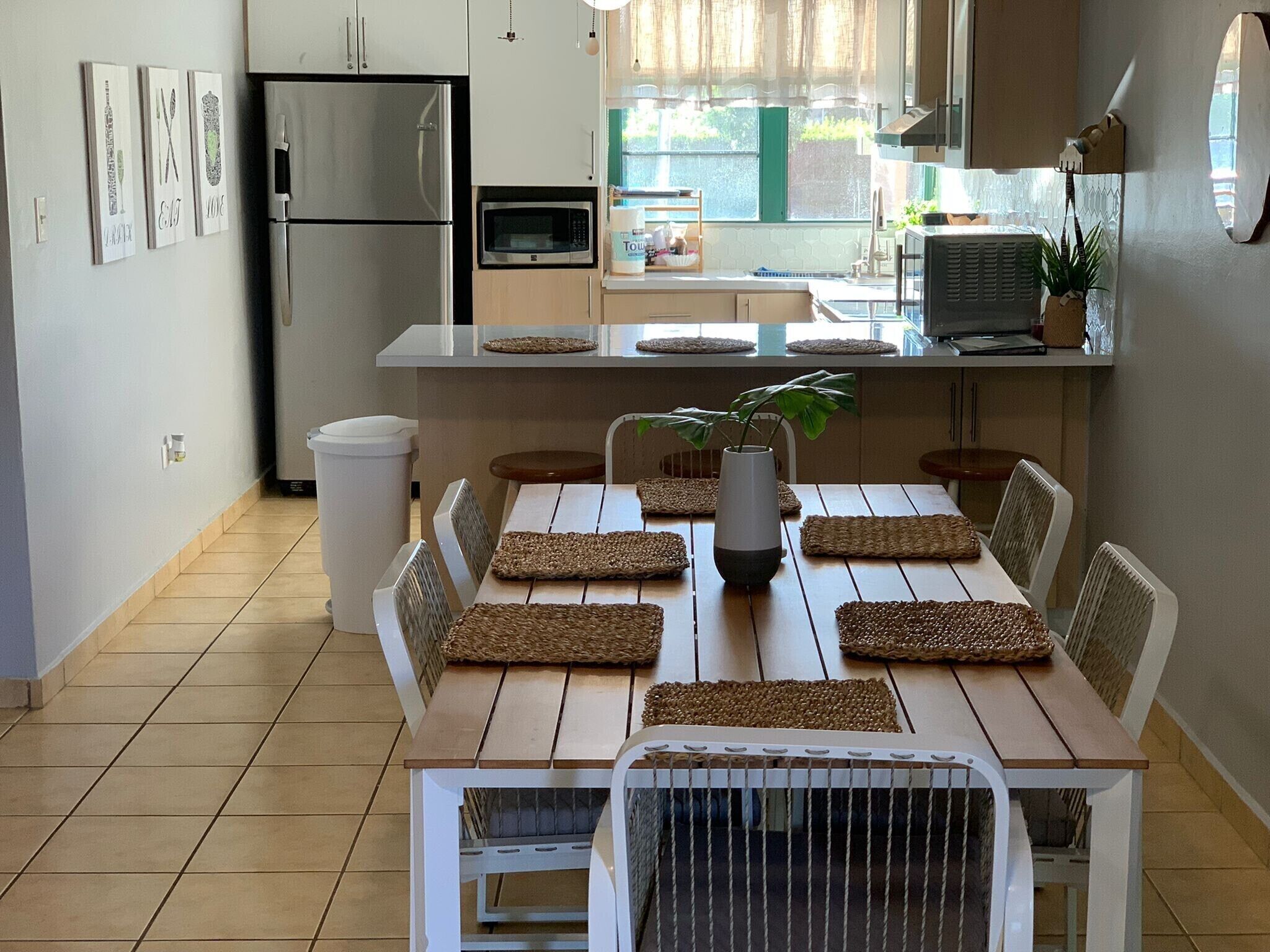 Une cuisine moderne dotée d’un îlot central, de meubles blancs et d’un coin repas avec une table et des chaises en bois.