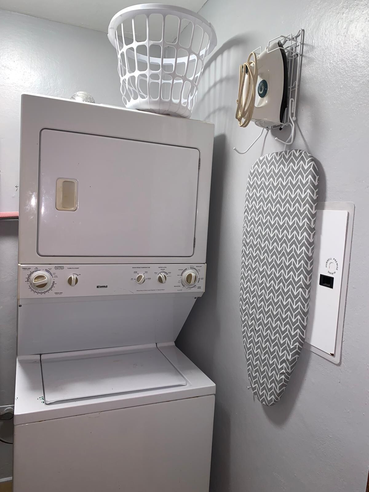 A compact laundry area with a washing machine, a drying rack, and a wall-mounted ironing board.