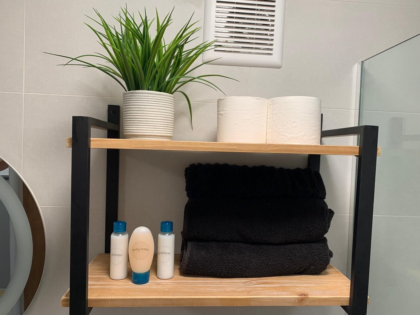 A bathroom shelf with a potted plant, rolled towels, and toiletries.