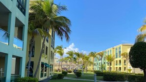 A courtyard with a pathway, palm trees, and a building with multiple floors and balconies. - Aquatika “A Cozy Paradise” (LOIZA)
