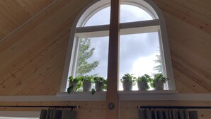 Una habitación con un alto techo de madera, un amplio ventanal de arco y plantas en macetas, y cortinas.