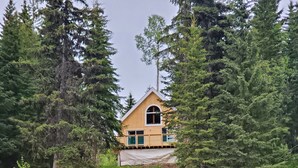 Una cabaña con un ventanal grande y una terraza, rodeada de un bosque frondoso y un lago tranquilo.