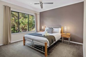 A bedroom with a bed, nightstands, a ceiling fan, and a large window with curtains.