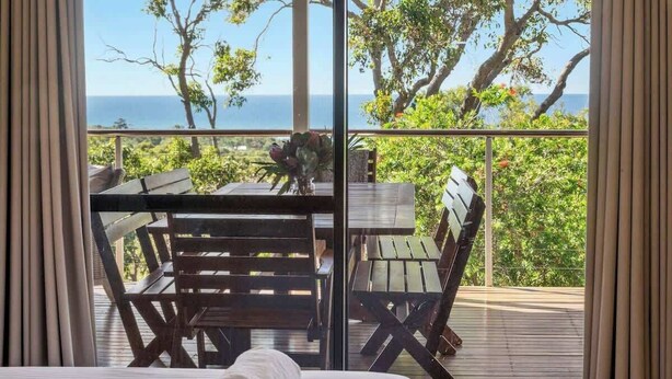 A balcony with a wooden table and chairs, a rolled towel, and a view of the ocean. - Eagle Vista—Beachside Bliss with Bushland Serenity (Eagle Bay)
