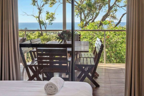 A balcony with a wooden table and chairs, a rolled towel, and a view of the ocean.