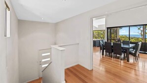 A modern interior with a staircase, a dining area with a table and chairs, and a view through large windows. - Eagle Vista—Beachside Bliss with Bushland Serenity (Eagle Bay)