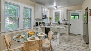 A modern kitchen with white cabinets, a built-in microwave, and a dining area with a glass table and wicker chairs.