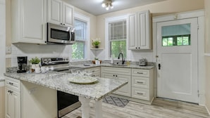 A kitchen with white cabinetry, a granite countertop, a stainless steel oven, a microwave, a sink, and a door with a frosted glass window.