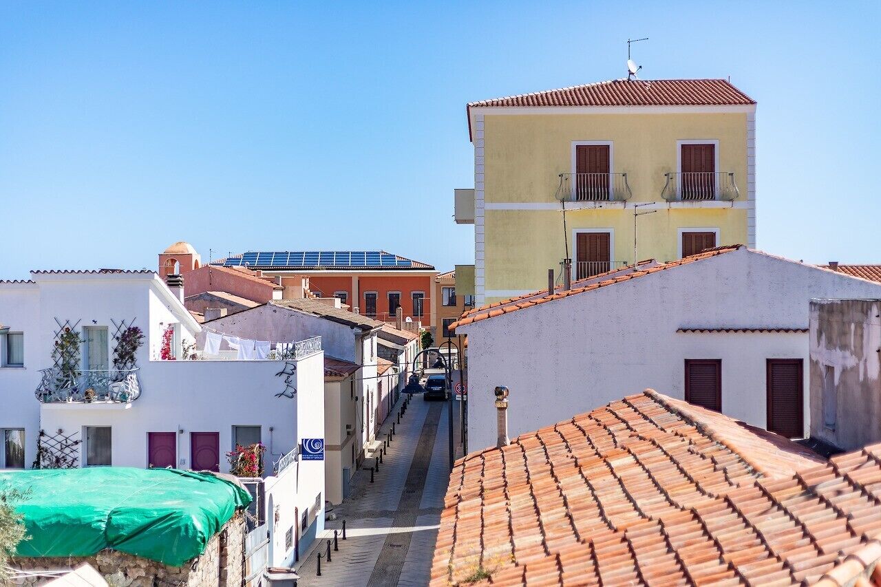 Une rue étroite bordée d’immeubles, dont certains sont dotés de balcons et de panneaux solaires.