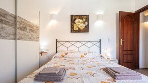 A bedroom with a bed, wall-mounted lights, a door, and a painting.