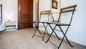 A room with a wooden door, a small bedside table with a lamp, and a foldable chair.