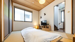 A bedroom with tatami flooring, a bed, a TV, and a sliding door leading to a staircase. - Urban Stay Shinagawa (Tokyo)